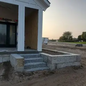 A building under construction with a dirt road and trees. This construction site features the 7" Dover Sawn Steps leading up to the entrance and a Capstone finishing touch.