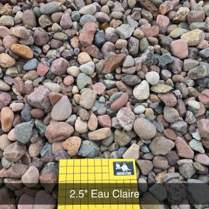 A large pile of smooth, multicolored rocks ranging from light gray to reddish-brown. A yellow grid board with "2.5" Eau Claire" and "1 inch squares" is positioned in front, providing scale and information.