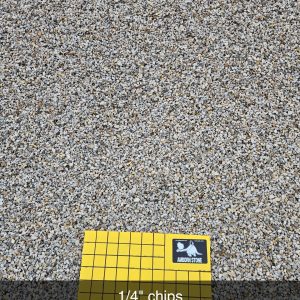 A sample of 1/4 inch gravel chips covers the ground. A yellow grid labeled "Armor Rock and Stone" with 1-inch squares is placed on top, demonstrating the scale of the gravel pieces.
